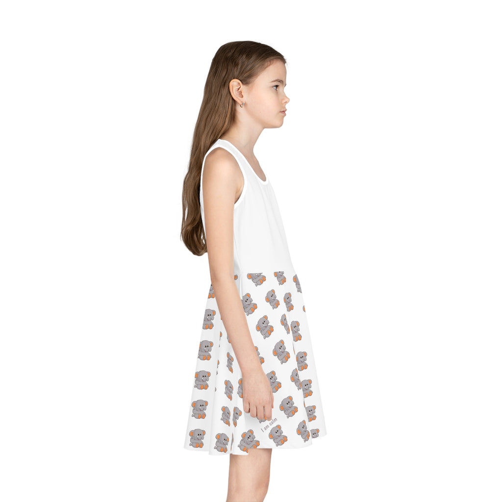 Right side-view of a girl wearing a sleeveless white dress with a white top and a repeating pattern of an elephant on the skirt.