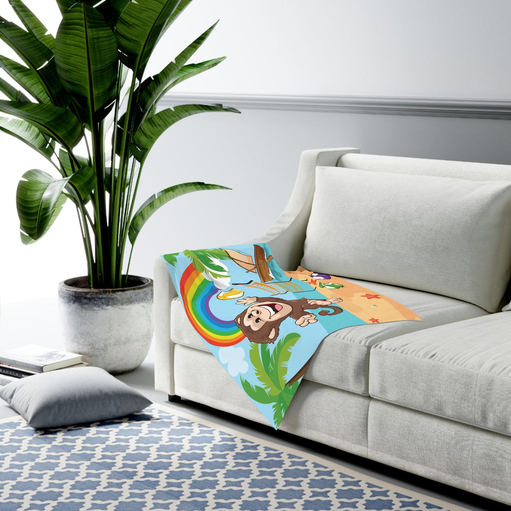 Full-color swaddle blanket with a monkey playing volleyball on a beach with a rainbow in the background. The blanket is draped over the armrest of a couch.