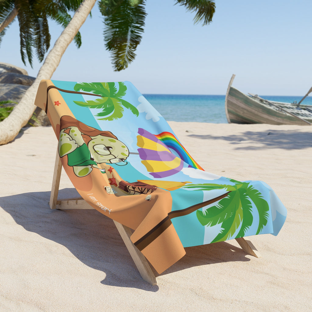 A 36 by 72 inch beach towel draped over a chair on a beach. The towel has a scene of a turtle reading a book under an umbrella on the beach, a rainbow in the background, and the phrase "I am smart" along the bottom.