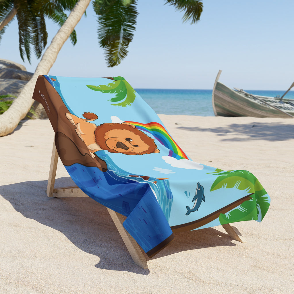A 36 by 72 inch beach towel draped over a chair on a beach. The towel has a scene of a lion standing on a cliff over the ocean, a rainbow in the background, and the phrase "I am strong" along the bottom.