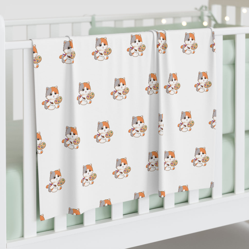 A white swaddle blanket with a repeating pattern of a cat. The blanket is draped over the side of a baby crib.