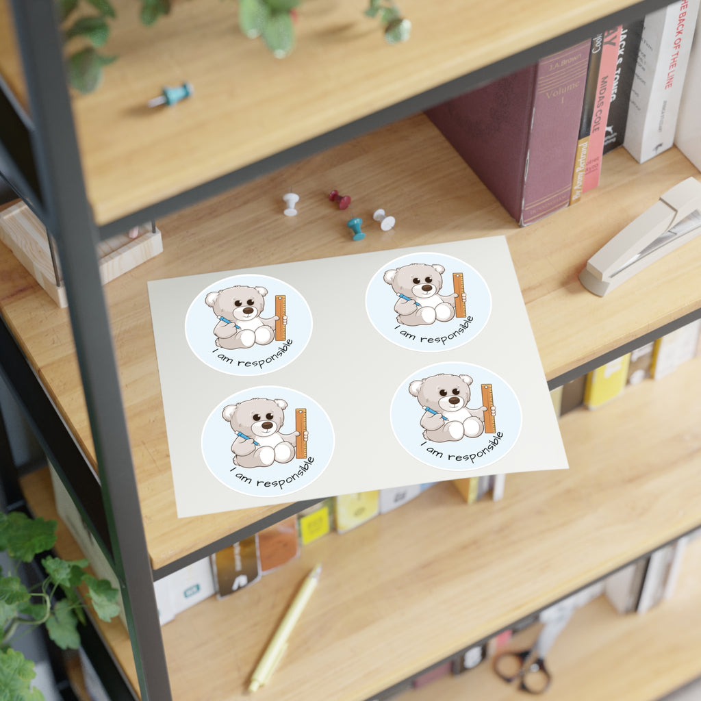 A sheet of 4 round stickers with a picture of a bear that says I am responsible. The sticker sheet sits on a shelf of a bookcase.