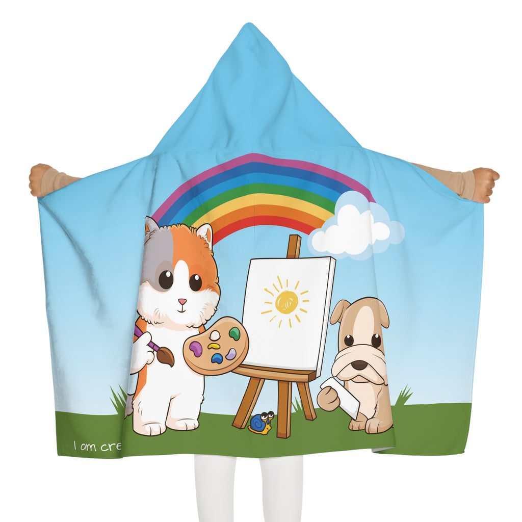 Back-view of a girl wearing a hooded towel and holding it open. The towel has a scene of a cat painting on a canvas next to a dog, a rainbow in the background, and the phrase "I am creative" along the bottom.