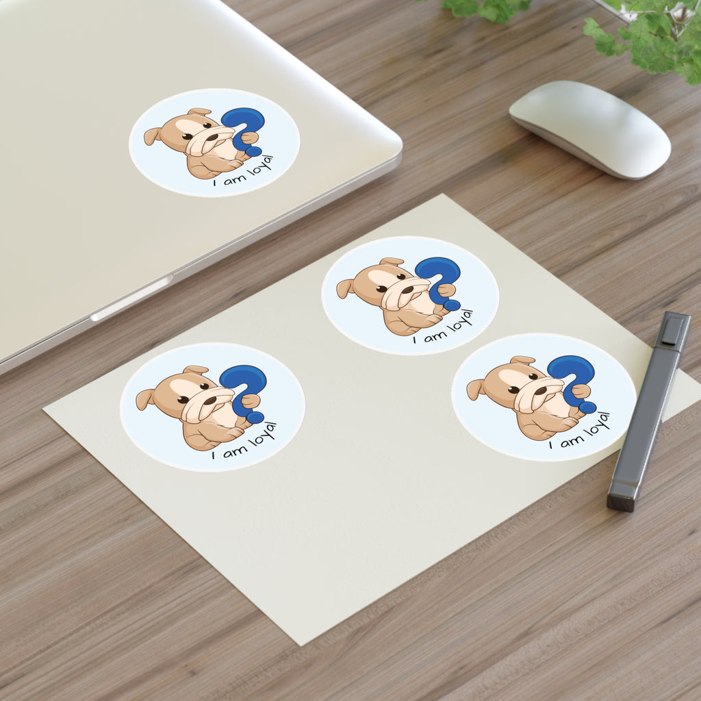 A sheet of 3 round stickers with a picture of a dog that says I am loyal. The sticker sheet sits on a table next to a laptop with the fourth sticker on it.