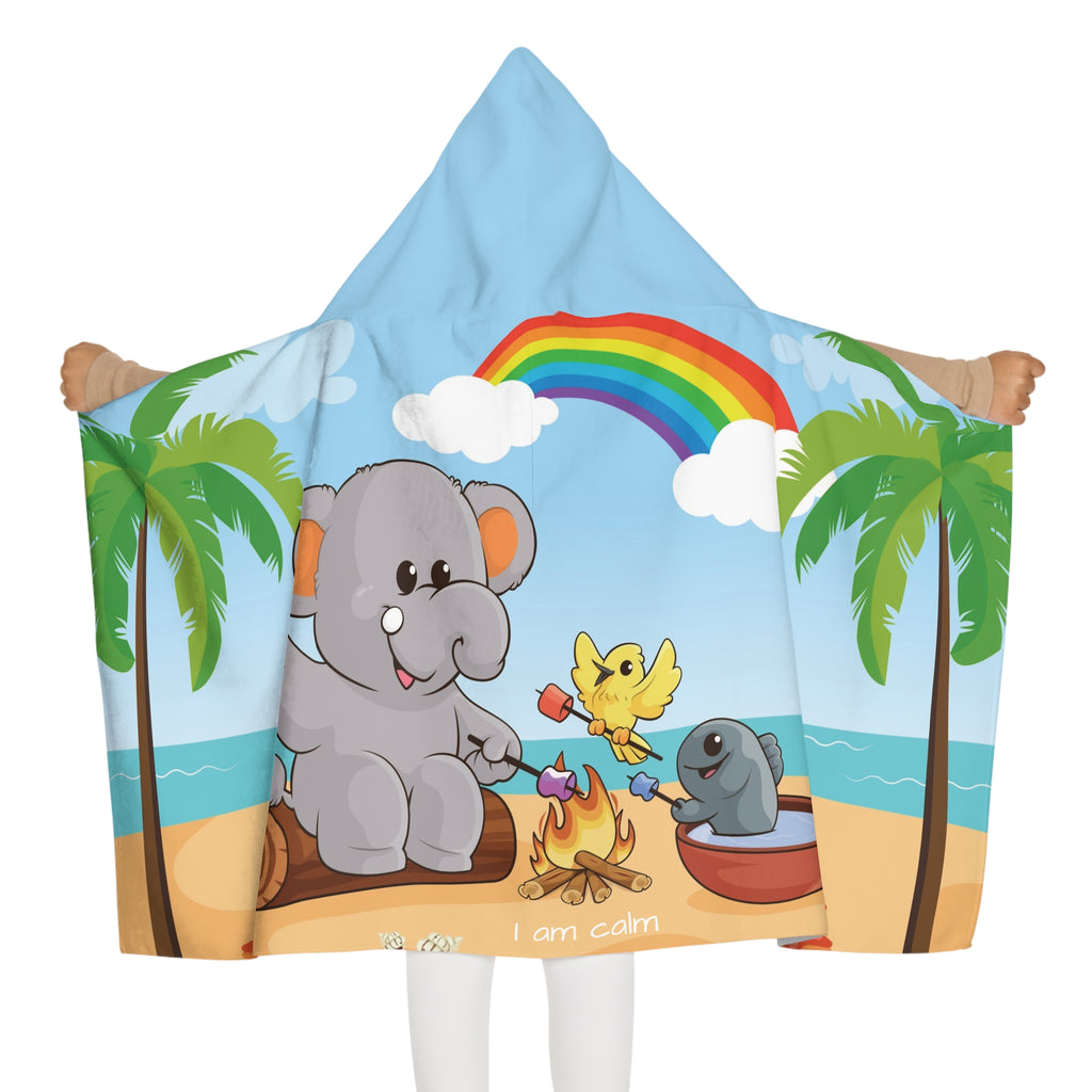 Back-view of a girl wearing a hooded towel and holding it open. The towel has a scene of an elephant having a bonfire with a bird and fish on the beach, a rainbow in the background, and the phrase "I am calm" along the bottom.
