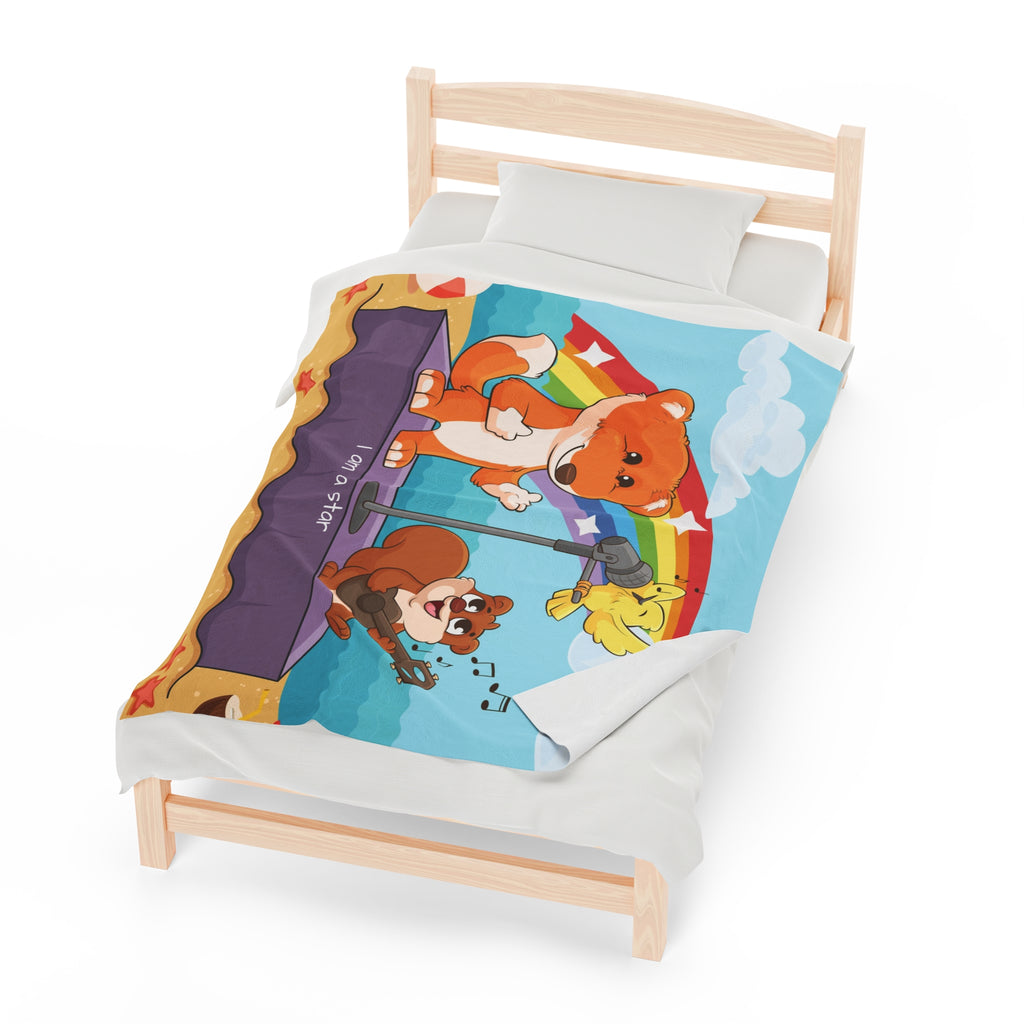 A 50 by 60 inch blanket on a twin-sized bed. The blanket has a scene of a fox singing with a bird and squirrel on a stage on the beach, a rainbow in the background, and the phrase "I am a star" along the bottom.