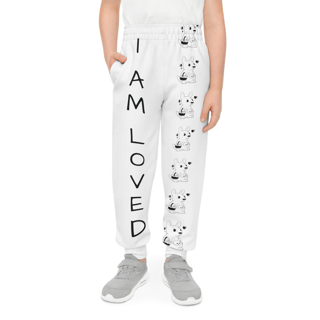 Front-view of a boy wearing white sweatpants with a line of black and white kangaroos down the front left leg and the phrase "I am loved" down the front right leg.