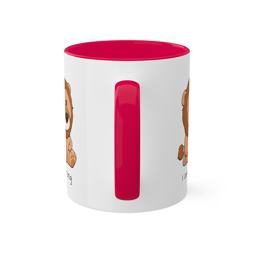 A white mug with a red handle and interior and a picture of a lion that says I am strong.