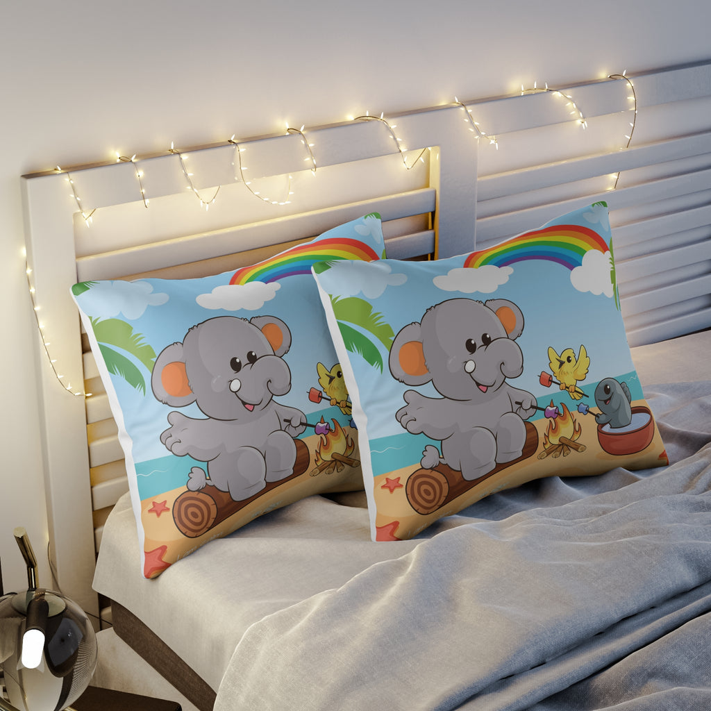 Two pillows sitting on a bed. The pillows have on pillowcases with a scene of an elephant having a bonfire with a bird and fish on the beach, a rainbow in the background, and the phrase "I am calm" along the bottom.