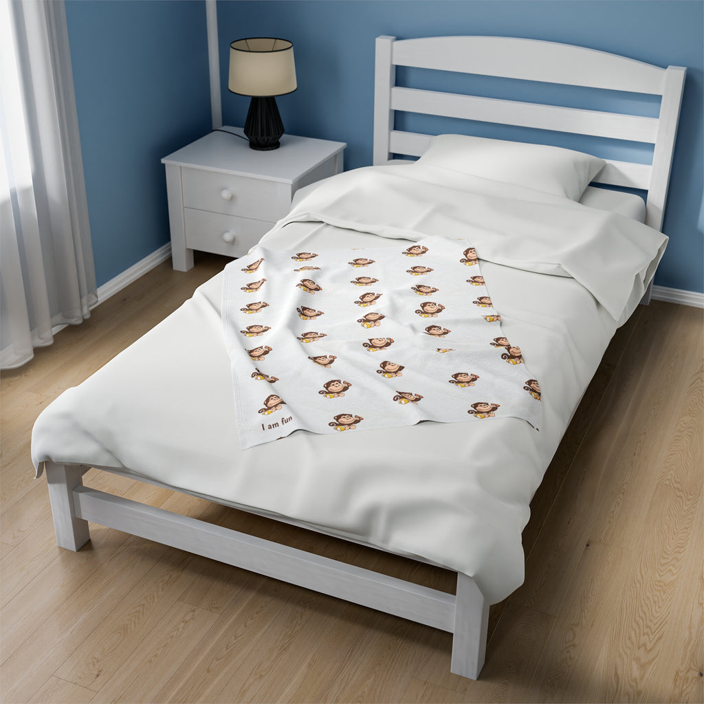 A 30 by 40 inch blanket on a twin-sized bed in a bedroom. The blanket has a repeating pattern of a monkey and the phrase “I am fun” in the bottom left corner.