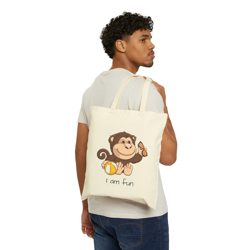 A man with a natural tan tote bag over his shoulder, featuring a picture of a monkey that says I am fun.