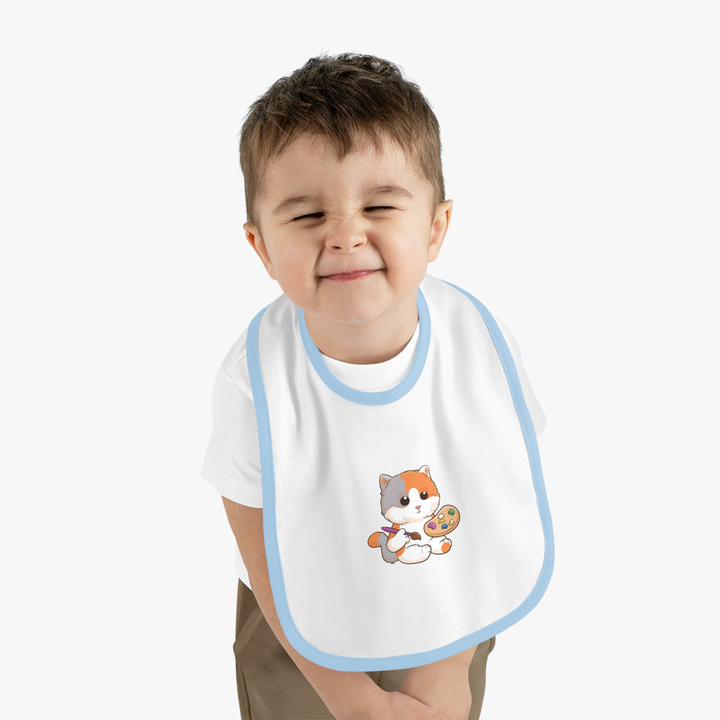 A little boy wearing a white baby bib with light blue trim and a small picture of a cat.
