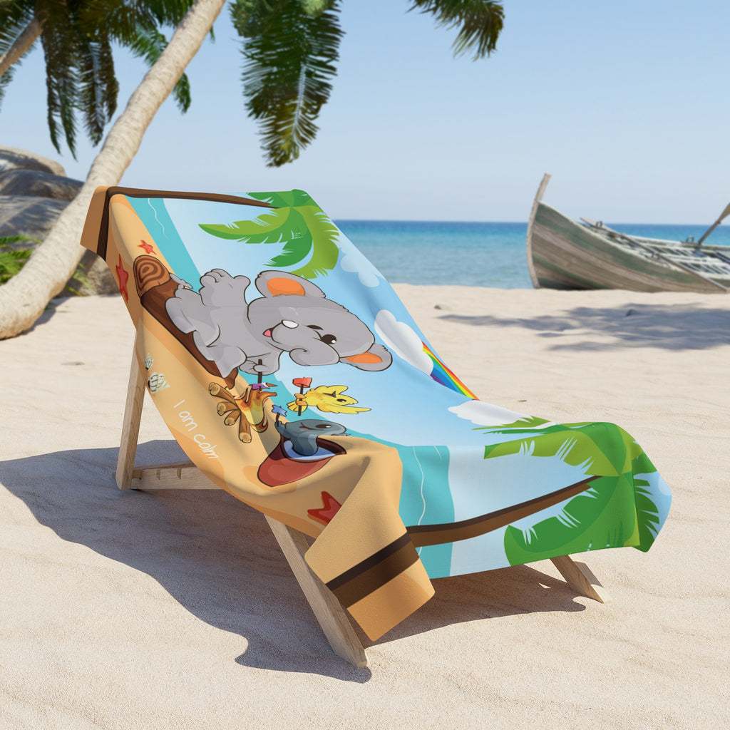 A 36 by 72 inch beach towel draped over a chair on a beach. The towel has a scene of an elephant having a bonfire with a bird and fish on the beach, a rainbow in the background, and the phrase "I am calm" along the bottom.