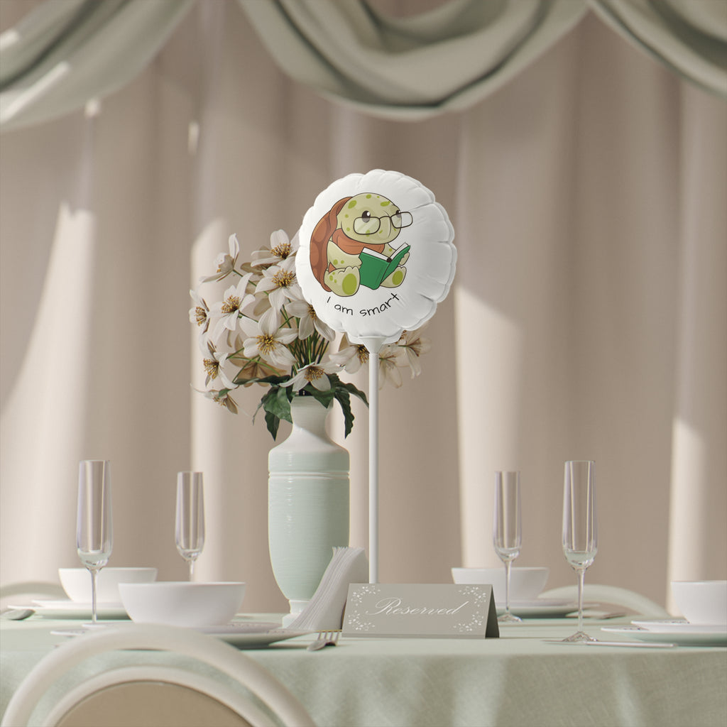 A round white mylar balloon on a stick with a picture of a turtle that says I am smart. The balloon sits on a table decorated for an event.