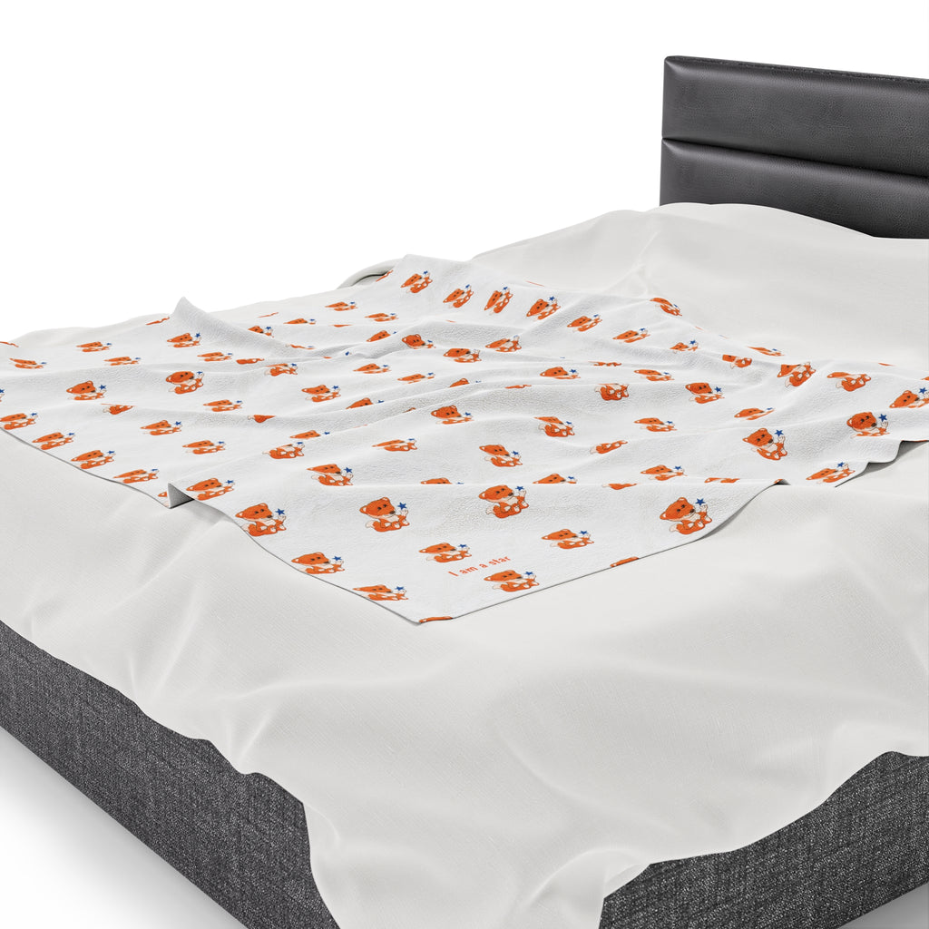 Side-view of a 50 by 60 inch blanket on a queen-sized bed. The blanket has a repeating pattern of a fox and the phrase “I am a star” in the bottom left corner.
