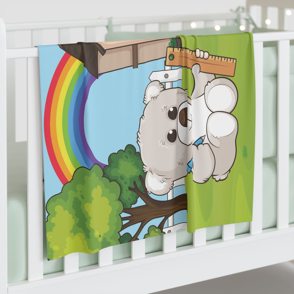 Full-color swaddle blanket with a bear sitting in the yard of its house with a rainbow in the background. The blanket is draped over the side of a baby crib.