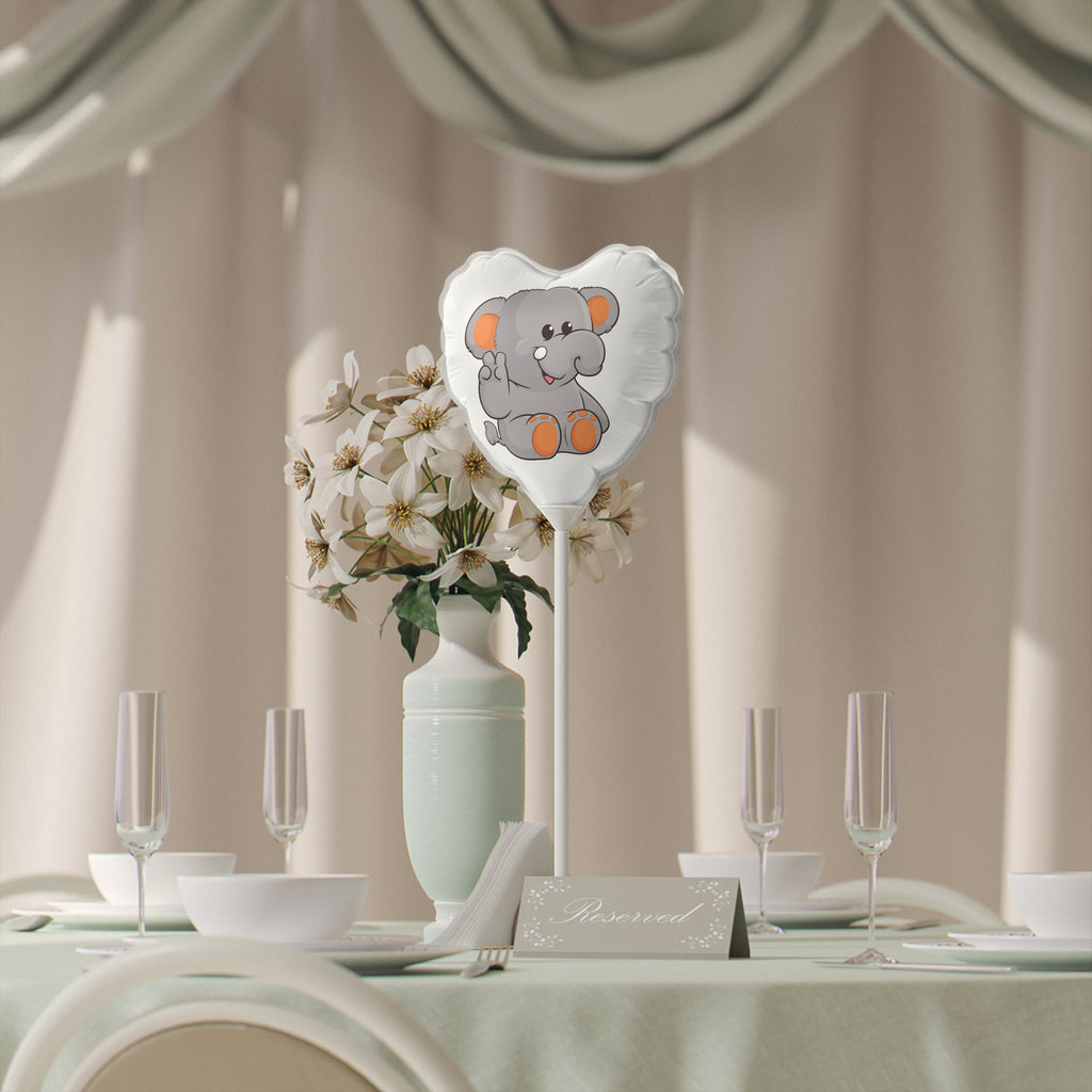 A heart-shaped white mylar balloon on a stick with a picture of an elephant. The balloon sits on a table decorated for an event.