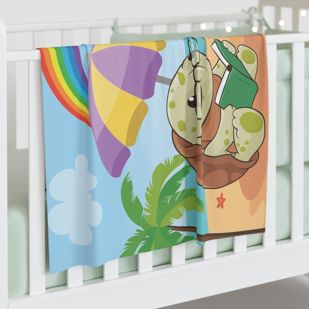 Full-color swaddle blanket with a turtle reading a book under an umbrella on a beach with a rainbow in the background. The blanket is draped over the side of a baby crib.