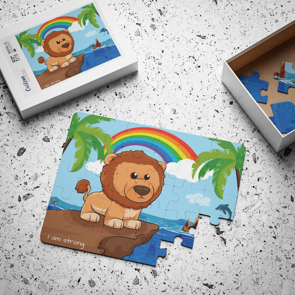 A 30 piece puzzle with a scene of a lion standing on a cliff over the ocean, a rainbow in the background, and the phrase "I am strong" along the bottom. The puzzle is mostly assembled next to its container box.