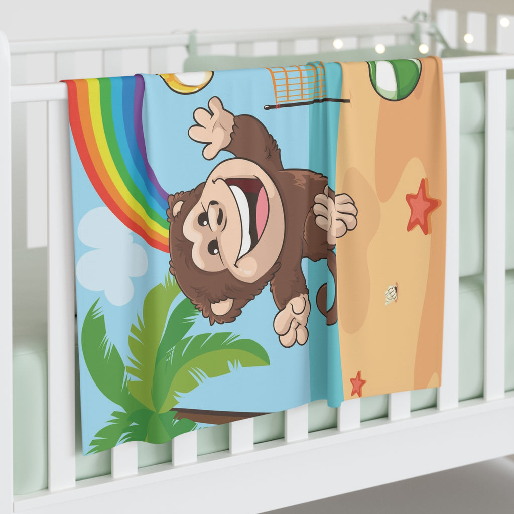 Full-color swaddle blanket with a monkey playing volleyball on a beach with a rainbow in the background. The blanket is draped over the side of a baby crib.