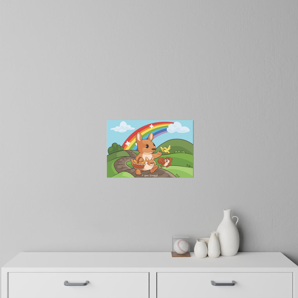 An 18 by 12 inch wall decal on a grey wall above a dresser. The wall decal has a scene of a kangaroo walking along a path through rolling hills, a rainbow in the background, and the phrase "I am loved" along the bottom.