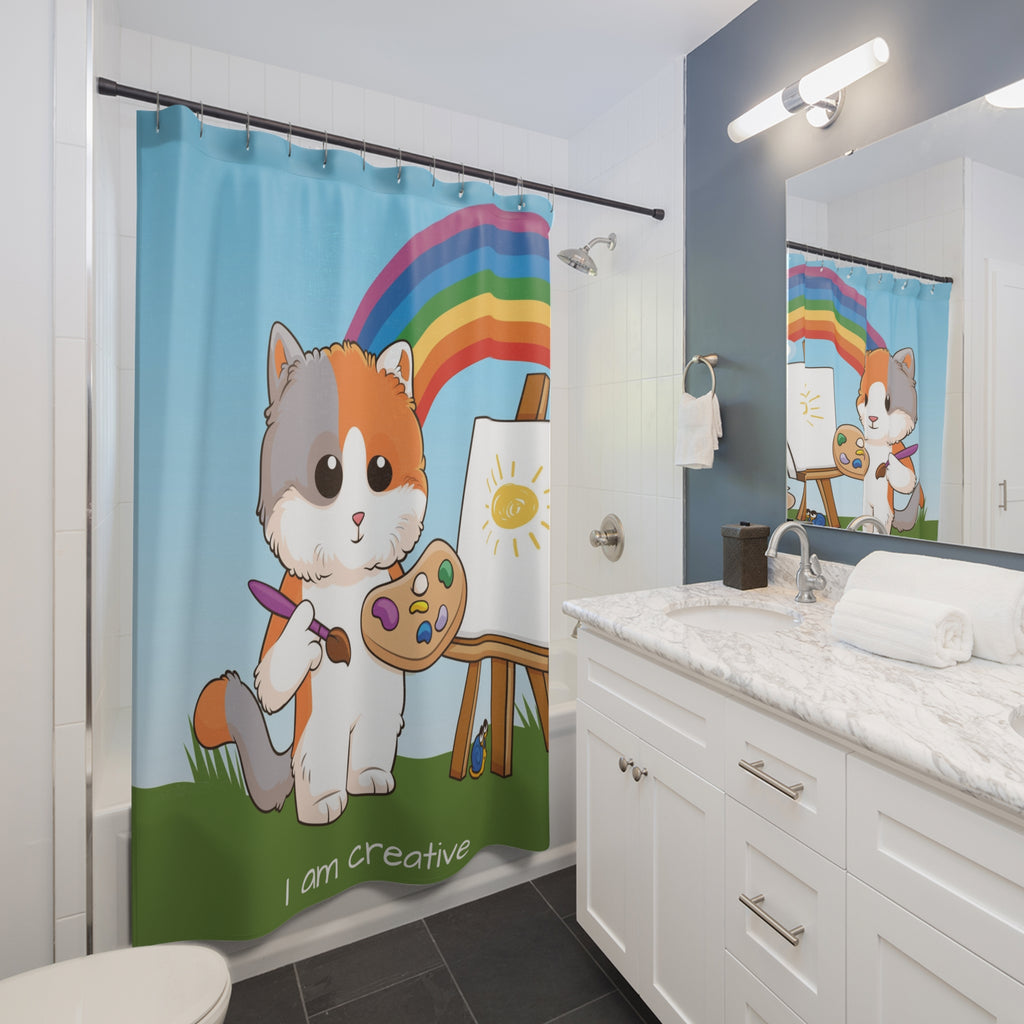 A shower curtain hanging from a rod in front of a built-in tub in a bathroom. The shower curtain has a scene of a cat painting on a canvas with a rainbow in the background and the phrase "I am creative" along the bottom.