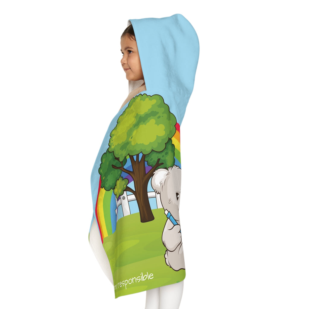 Left side-view of a girl wearing a hooded towel and holding it closed around her. The towel has a scene of a bear sitting in the yard of its house, a rainbow in the background, and the phrase "I am responsible" along the bottom.