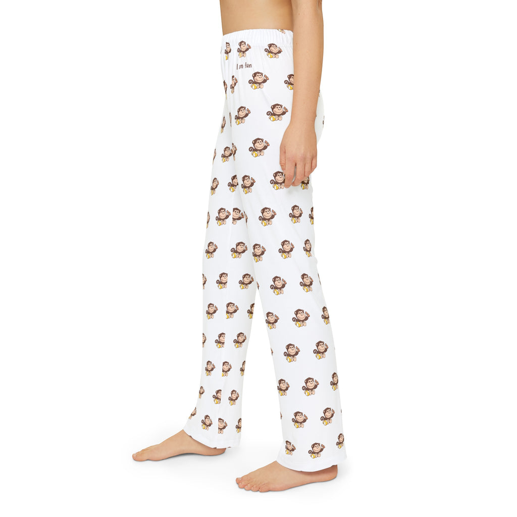 Left side-view of a kid wearing white pajama pants with a repeated pattern of a monkey and the phrase “I am fun” on the front left waist.