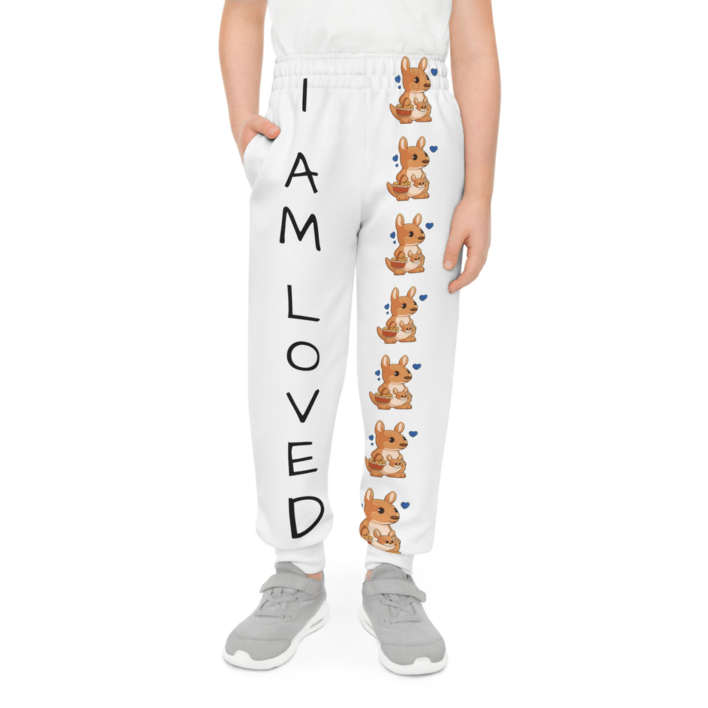 Front-view of a boy wearing white sweatpants with a line of kangaroos down the front left leg and the phrase "I am loved" down the front right leg.