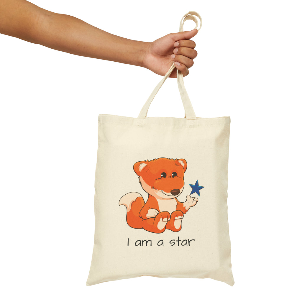 A hand holding a natural tan tote bag with a picture of a fox that says I am a star.