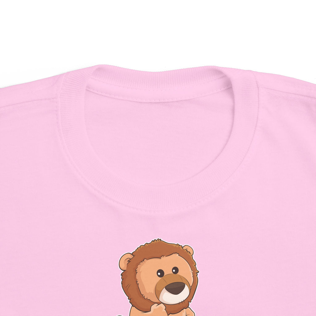 A close-up of the crew neckline of a short-sleeve light pink shirt with a picture of a lion that says I Got This.
