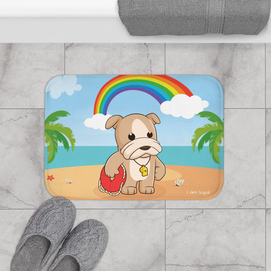A 24 by 17 inch bath mat on the tiled floor of a bathroom. The bath mat has a scene of a dog lifeguard standing on a beach with a rainbow in the background and the phrase "I am loyal" along the bottom.