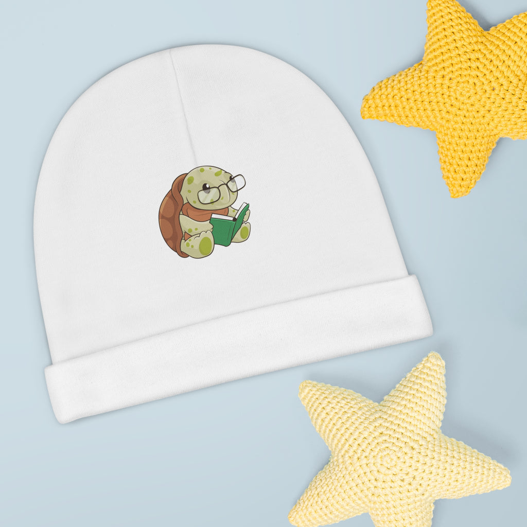 A white baby beanie with a small picture of a turtle. The beanie has the bottom edge folded up.