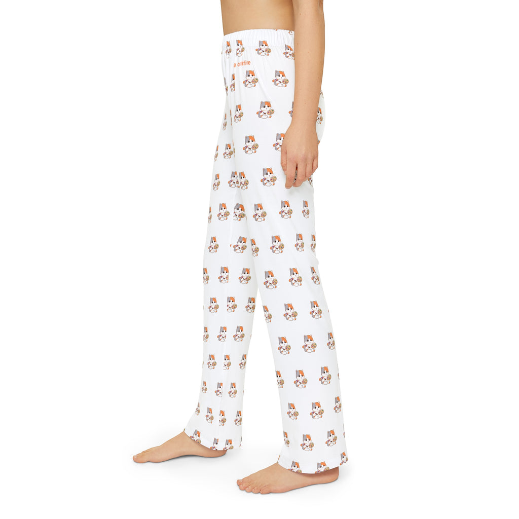 Left side-view of a kid wearing white pajama pants with a repeated pattern of a cat and the phrase “I am creative” on the front left waist.
