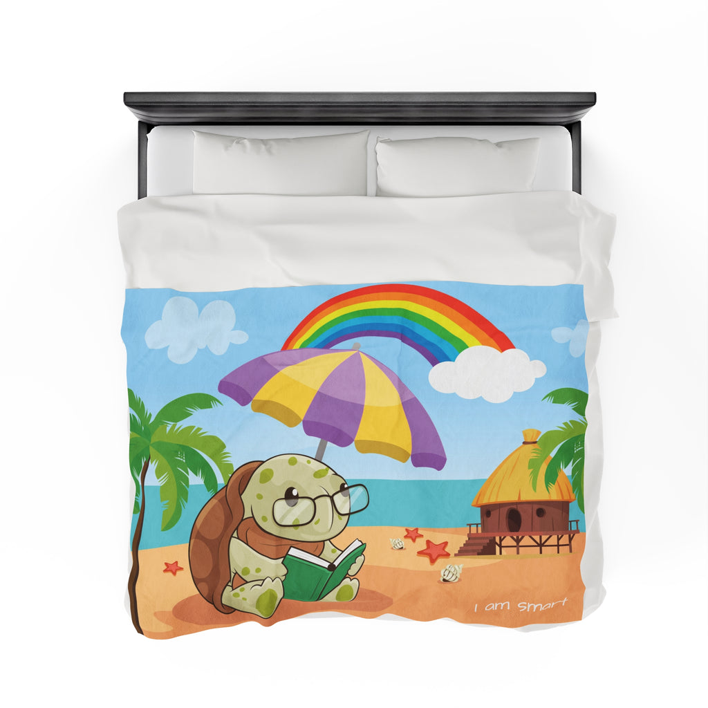 Top-view of a 60 by 80 inch blanket on a queen-sized bed. The blanket has a scene of a turtle reading under an umbrella on the beach, a rainbow in the background, and the phrase "I am smart" along the bottom.