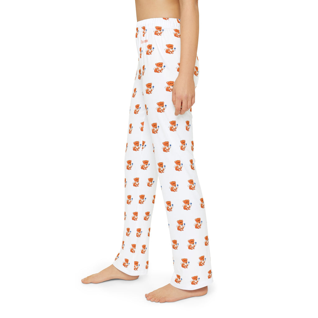 Left side-view of a kid wearing white pajama pants with a repeated pattern of a fox and the phrase “I am a star” on the front left waist.