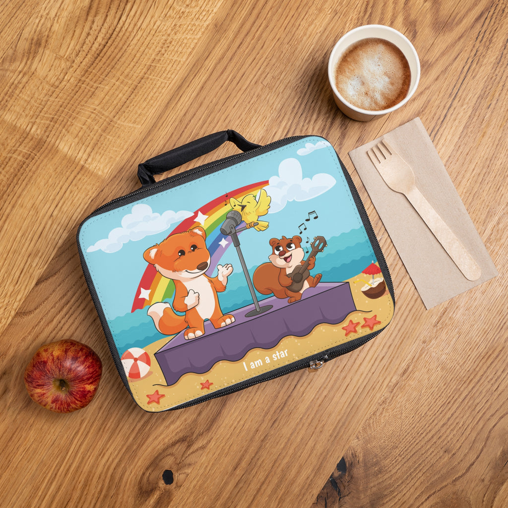 A lunch bag laying closed on a table next to a cup, fork, and apple. The lunch bag has a scene on the front of a fox singing with a bird and squirrel on a stage on the beach, a rainbow in the background, and the phrase "I am a star" along the bottom.