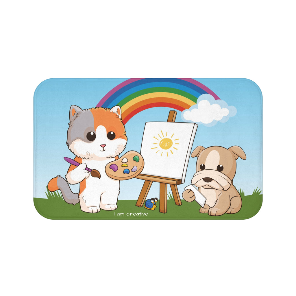 A 34 by 21 inch bath mat that has a scene of a cat painting on a canvas next to a dog with a rainbow in the background and the phrase "I am creative" along the bottom.