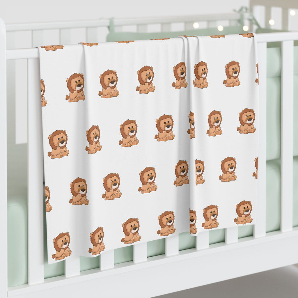 A white swaddle blanket with a repeating pattern of a lion. The blanket is draped over the side of a baby crib.