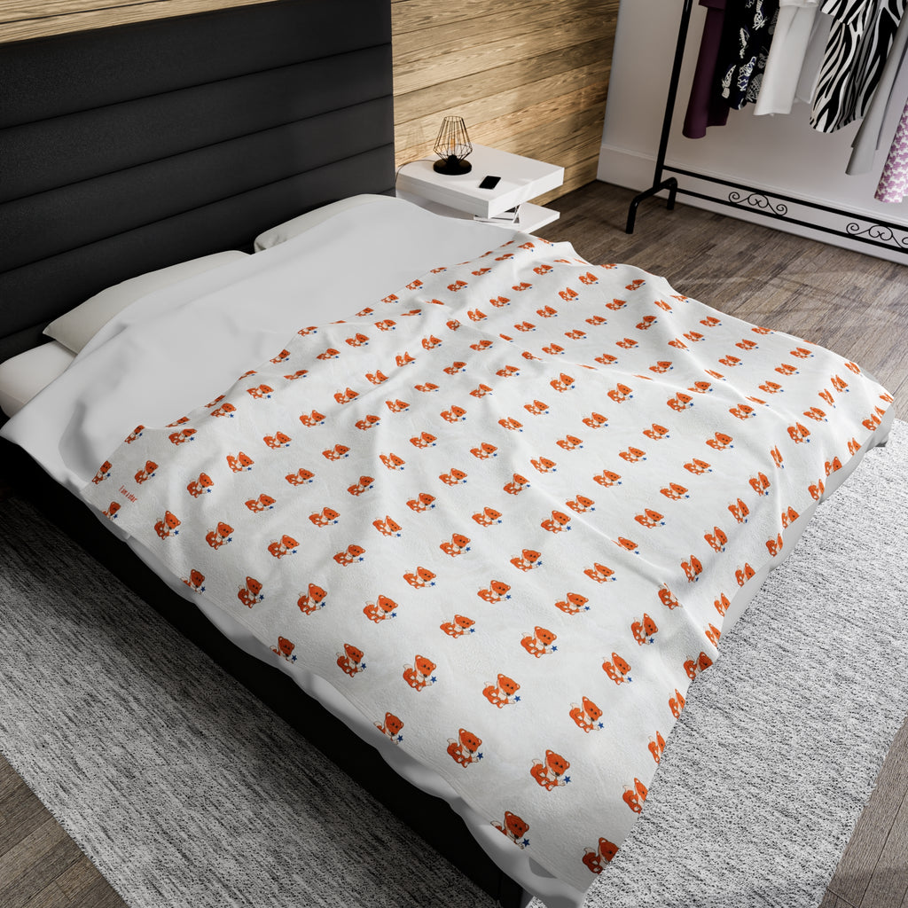 A 60 by 80 inch blanket on a queen-sized bed in a bedroom. The blanket has a repeating pattern of a fox and the phrase “I am a star” in the bottom left corner.