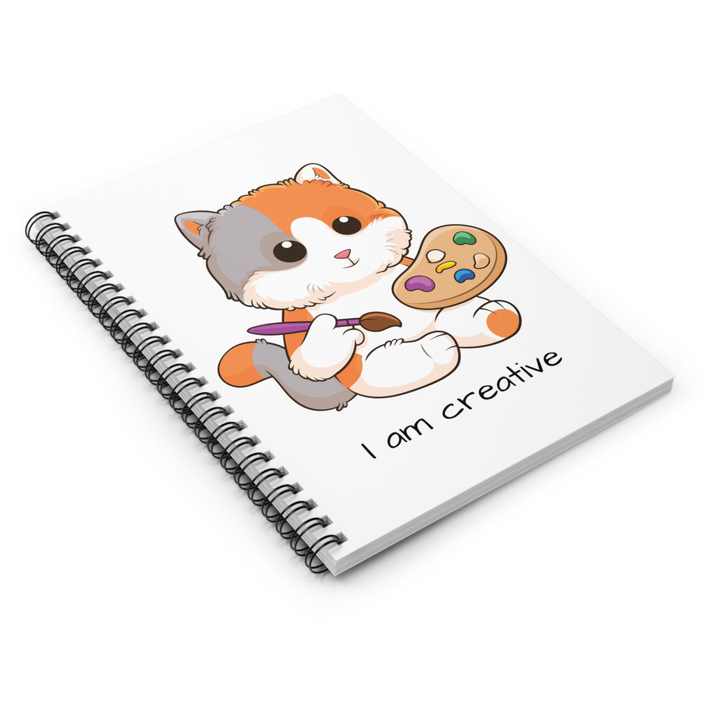 Side-view of a white spiral notebook laying closed, featuring a picture of a cat that says I am creative.