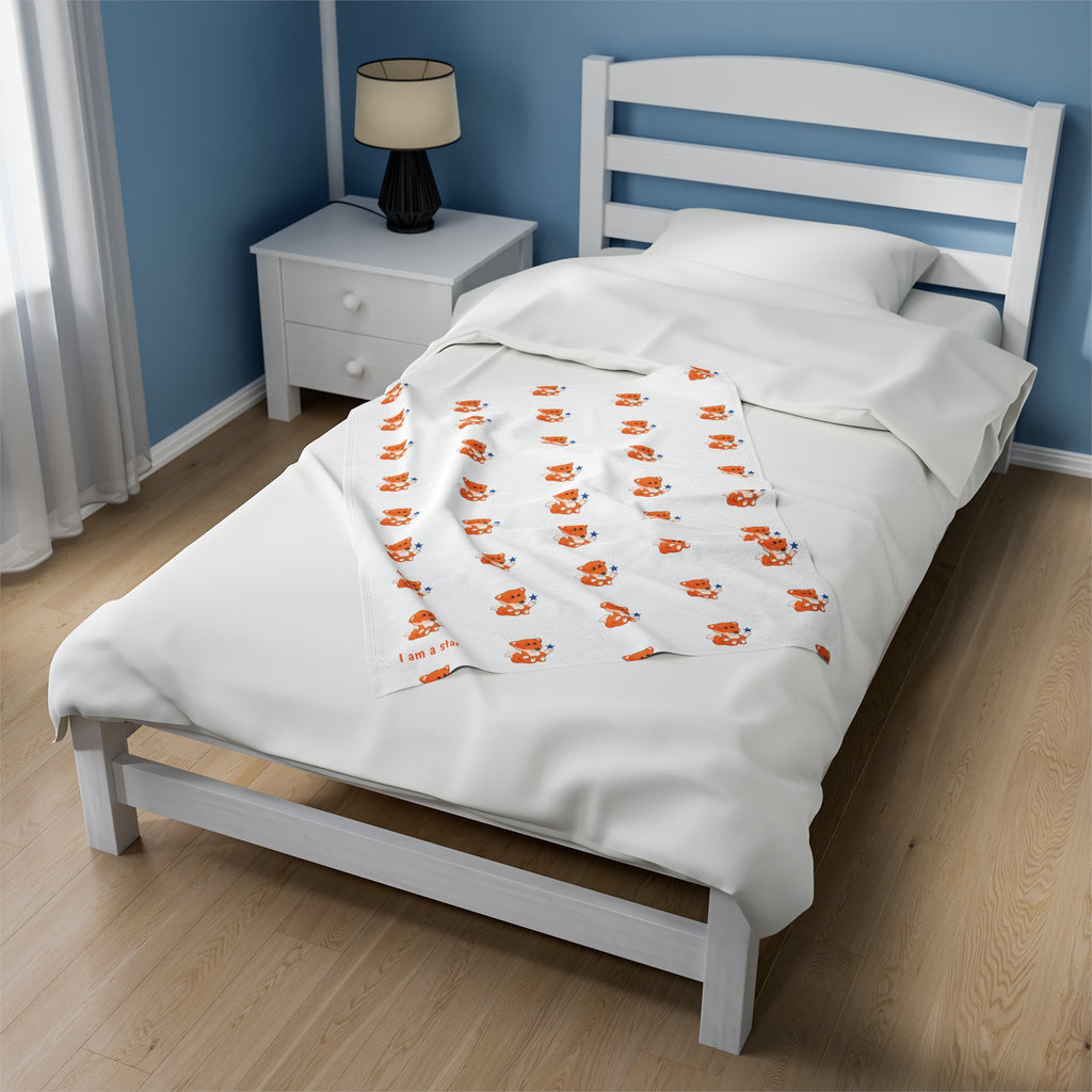 A 30 by 40 inch blanket on a twin-sized bed in a bedroom. The blanket has a repeating pattern of a fox and the phrase “I am a star” in the bottom left corner.