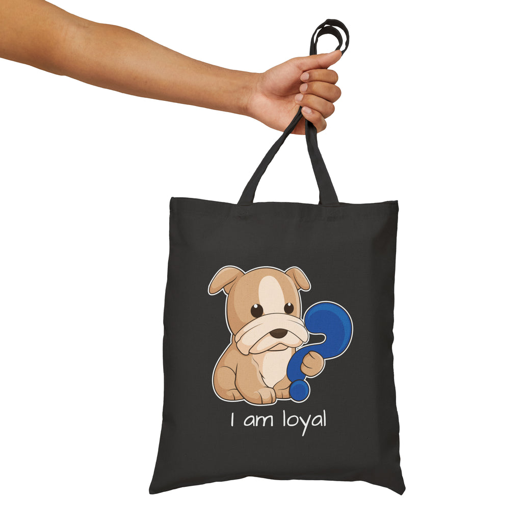 A hand holding a black tote bag with a picture of a dog that says I am loyal.