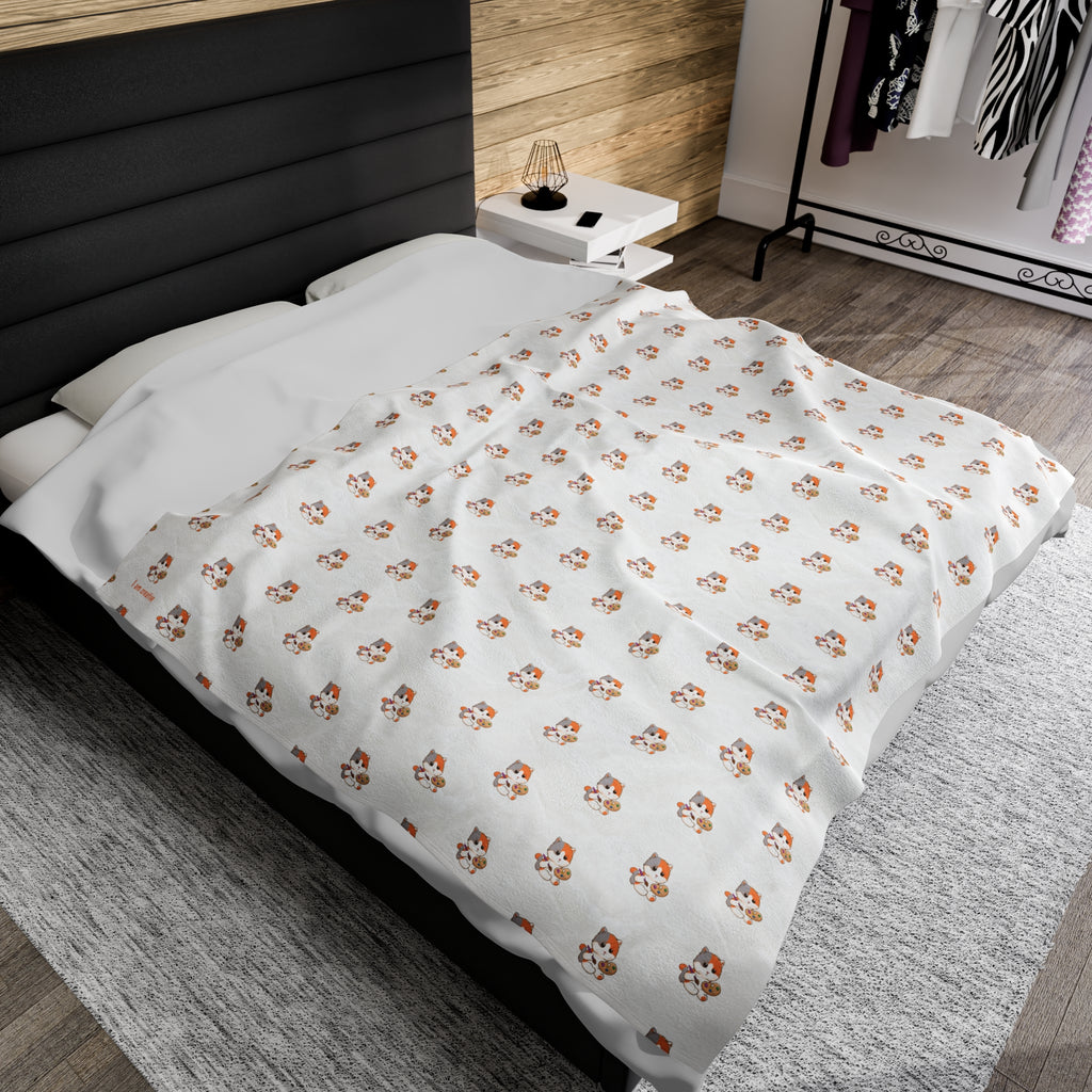 A 60 by 80 inch blanket on a queen-sized bed in a bedroom. The blanket has a repeating pattern of a cat and the phrase “I am creative” in the bottom left corner.