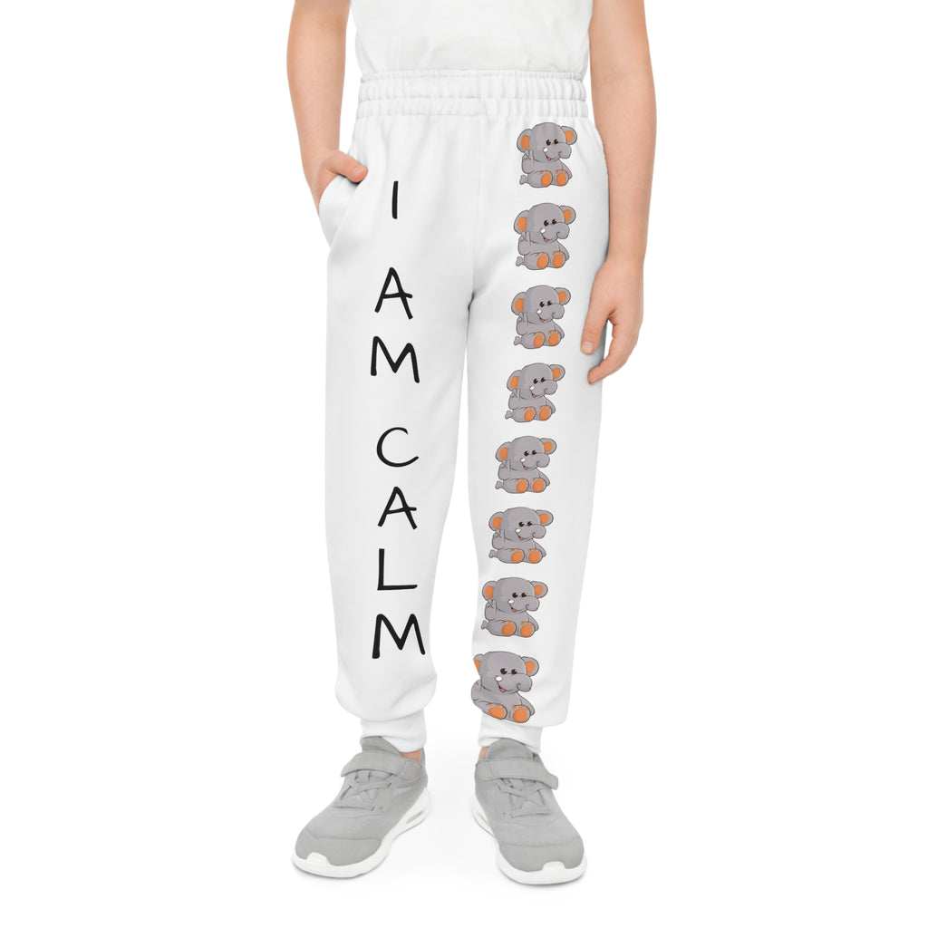 Front-view of a boy wearing white sweatpants with a line of elephants down the front left leg and the phrase "I am calm" down the front right leg.
