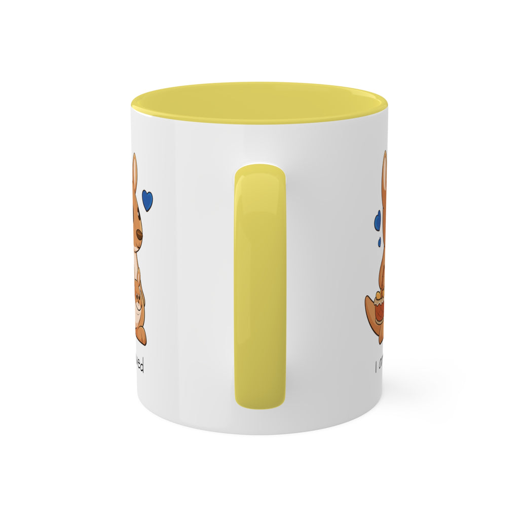A white mug with a yellow handle and interior and a picture of a kangaroo that says I am loved.