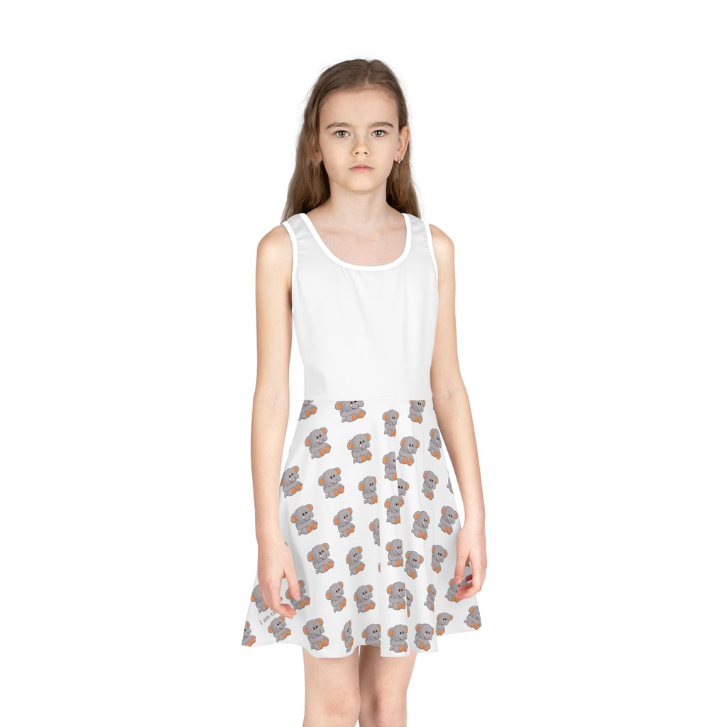Front-view of a girl wearing a sleeveless white dress with a white top and a repeating pattern of an elephant on the skirt.