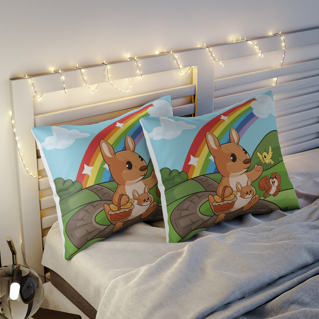 Two pillows sitting on a bed. The pillows have on pillowcases with a scene of a kangaroo walking along a path through rolling hills, a rainbow in the background, and the phrase "I am loved" along the bottom.