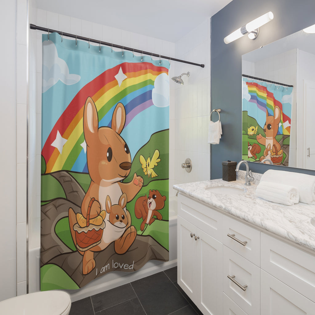 A shower curtain hanging from a rod in front of a built-in tub in a bathroom. The shower curtain has a scene of a kangaroo walking on a path through rolling hills with a rainbow in the background and the phrase "I am loved" along the bottom.