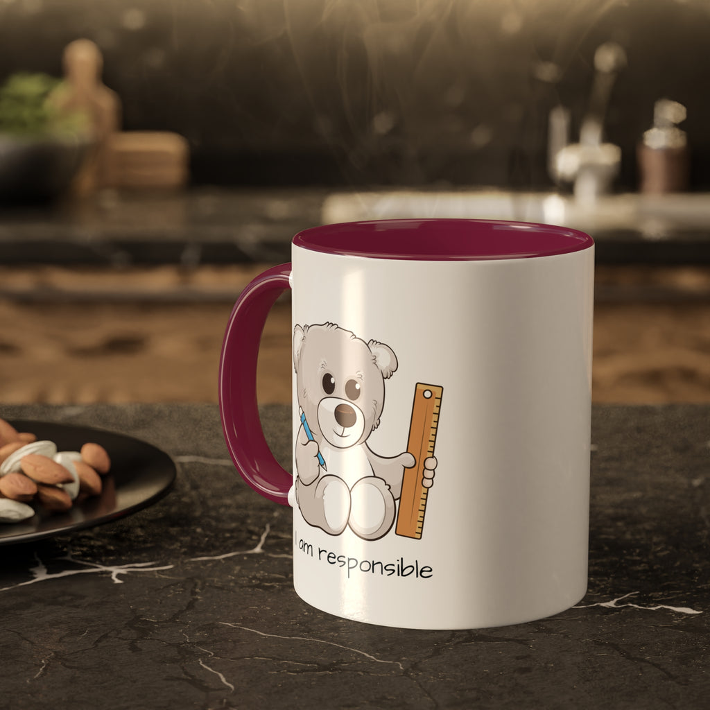 A white mug with a maroon handle and interior and a picture of a bear that says I am responsible. The mug sits on a black kitchen counter and has steam rising out of it.